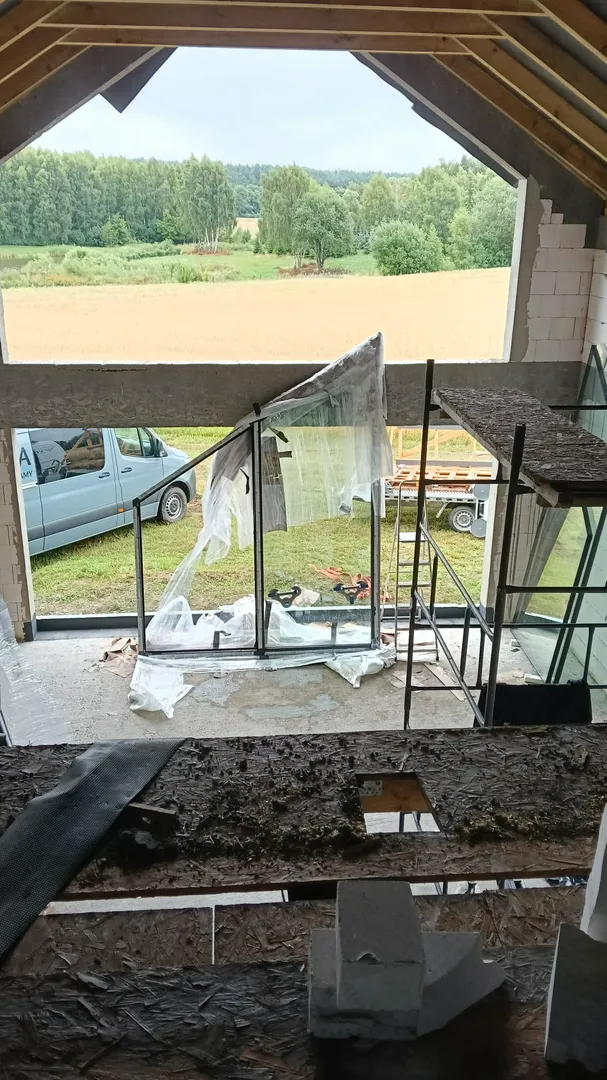 Surowe wnętrze z rusztowaniem i montażem okien tarasowych z widokiem na pole