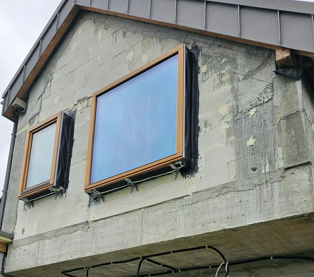 Surowa betonowa elewacja z dwoma zamontowanymi oknami w drewnianych ramach – Montaż okien