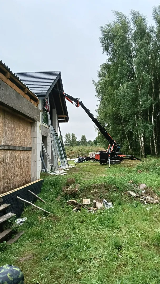 Montaż okien - pneumatyczny dźwig podnosi i umieszcza duże białe okno w otworze elewacyjnym