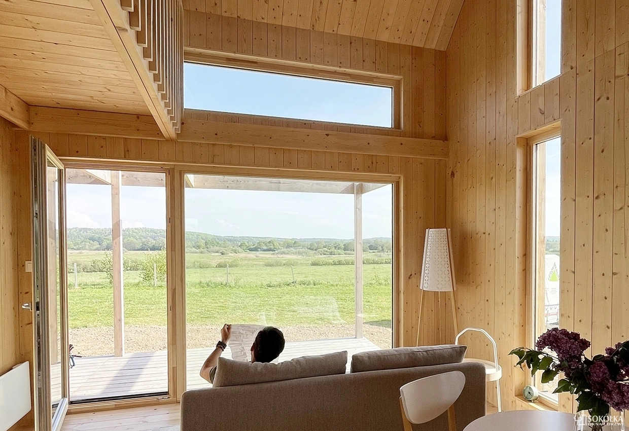 Duży salon z drewnianą boazerią wyposażony w Okna tarasowe z widokiem na zielone pola