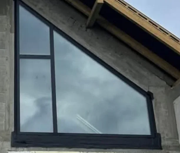 Trójkątne okno wielkoformatowe zamontowane w surowej betonowej elewacji pod dwuspadowym dachem