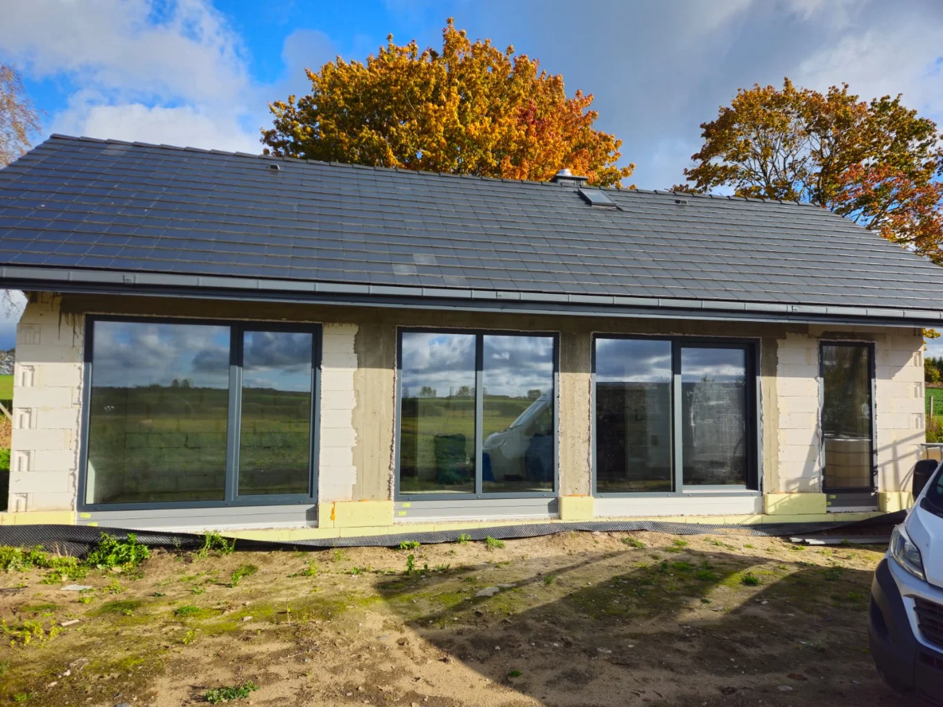 Okna wielkoformatowe zamontowane w elewacji domu w budowie z widokiem na otoczenie