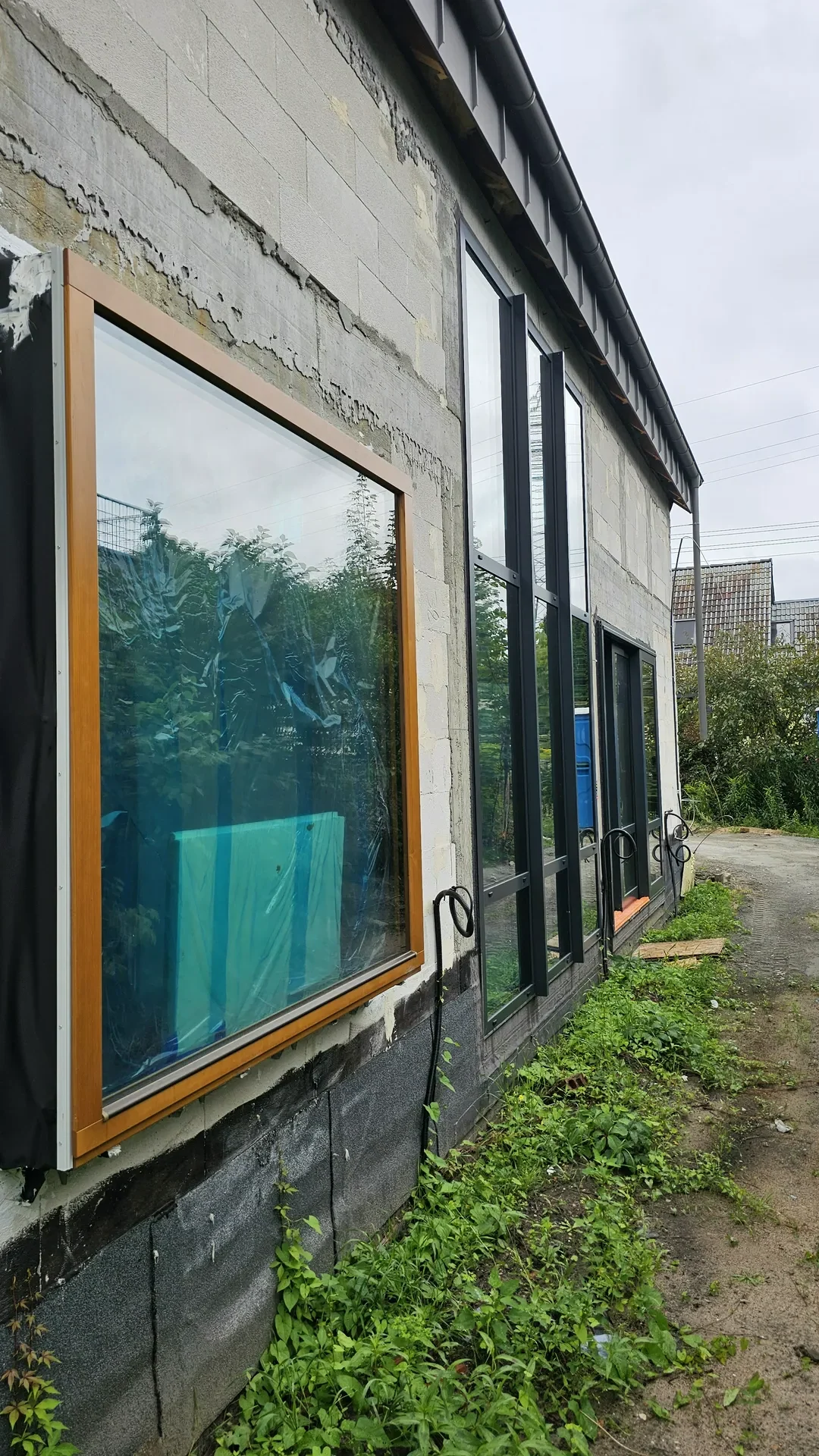 Czarne, aluminiowe okna wielkoformatowe zamontowane w surowej, niedokończonej elewacji budynku