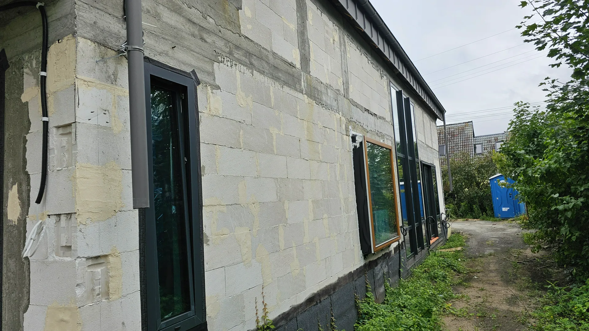 Montaż okien w surowej elewacji z bloczków, duże czarne ramy okienne na parterze budynku