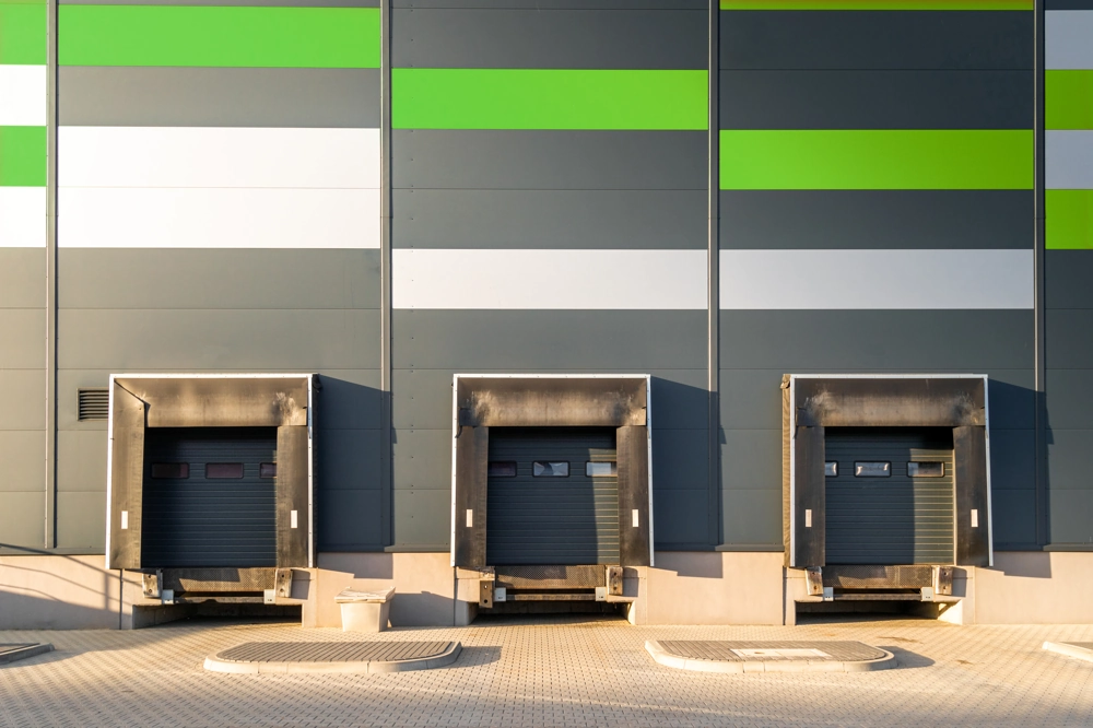 Trzy stanowiska przeładunkowe z segmentowymi bramami przemysłowymi w elewacji magazynu