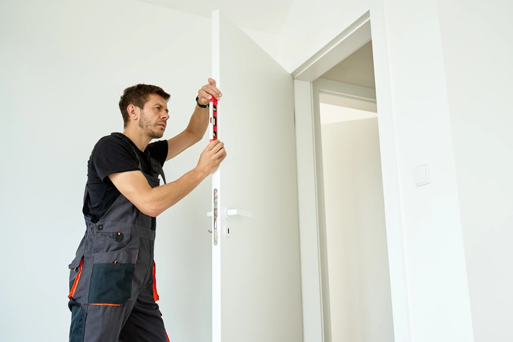 Montaż drzwi: pracownik poziomujący ościeżnicę białych drzwi wewnętrznych w jasnym pomieszczeniu
