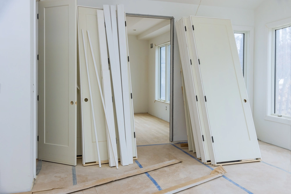 Kilka białych drzwi i listew ościeżnic uporządkowanych na podłodze w pustym wnętrzu Montaż drzwi