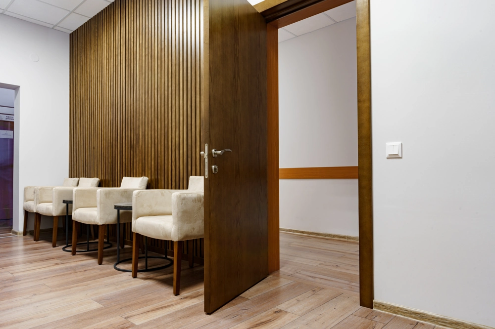 Otwierane drewniane drzwi wewnętrzne z widokiem na poczekalnię z tapicerowanymi fotelami Drzwi drewniane