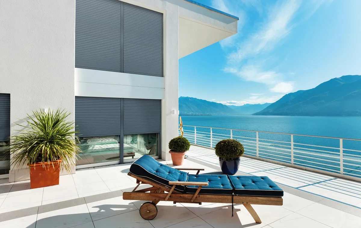 Białe okna tarasowe w nowoczesnym domu z tarasem nad jeziorem i leżakiem