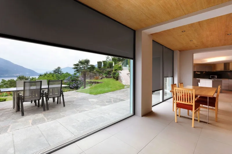 Rolety screen zamontowane na przeszklonych drzwiach tarasowych z widokiem na ogród i jezioro