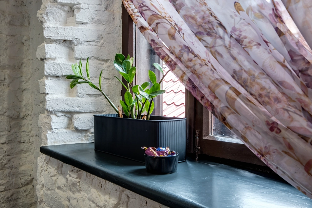 Parapety wewnętrzne – czarny parapet z doniczką i zasłoną przy oknie