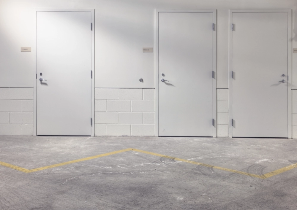 Trzy białe drzwi stalowe w magazynowym korytarzu z betonową podłogą i żółtą linią